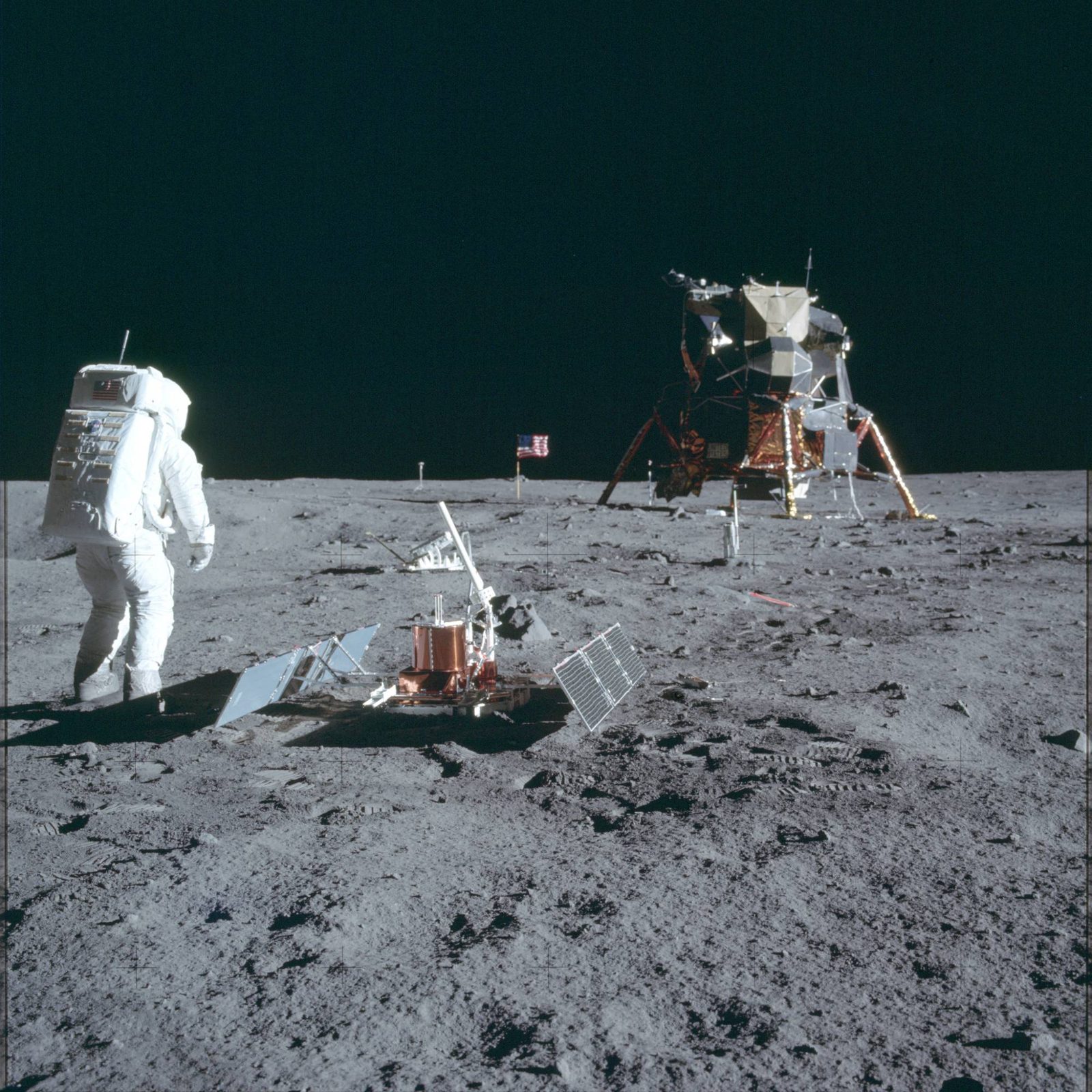 Aldrin beside the deployed Passive Seismic Experiment Package; the LRRR, U.S. flag, and the LM are also in frame (AS11-40-5948, NASA).